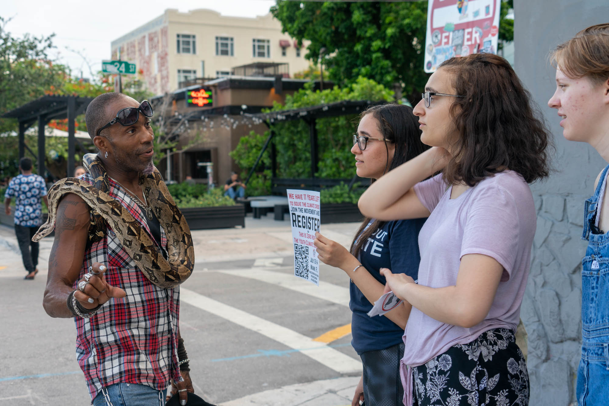 Ray “Fangdaddy” Henry, a street performer in Miami’s Wynwood Walls district, learns about the Youth Climate Summit from Zero Hour activists (from left) Sohayla Eldeeb, Jamie Margolin and Kendall Kieras. (Jordan Laird/News21)