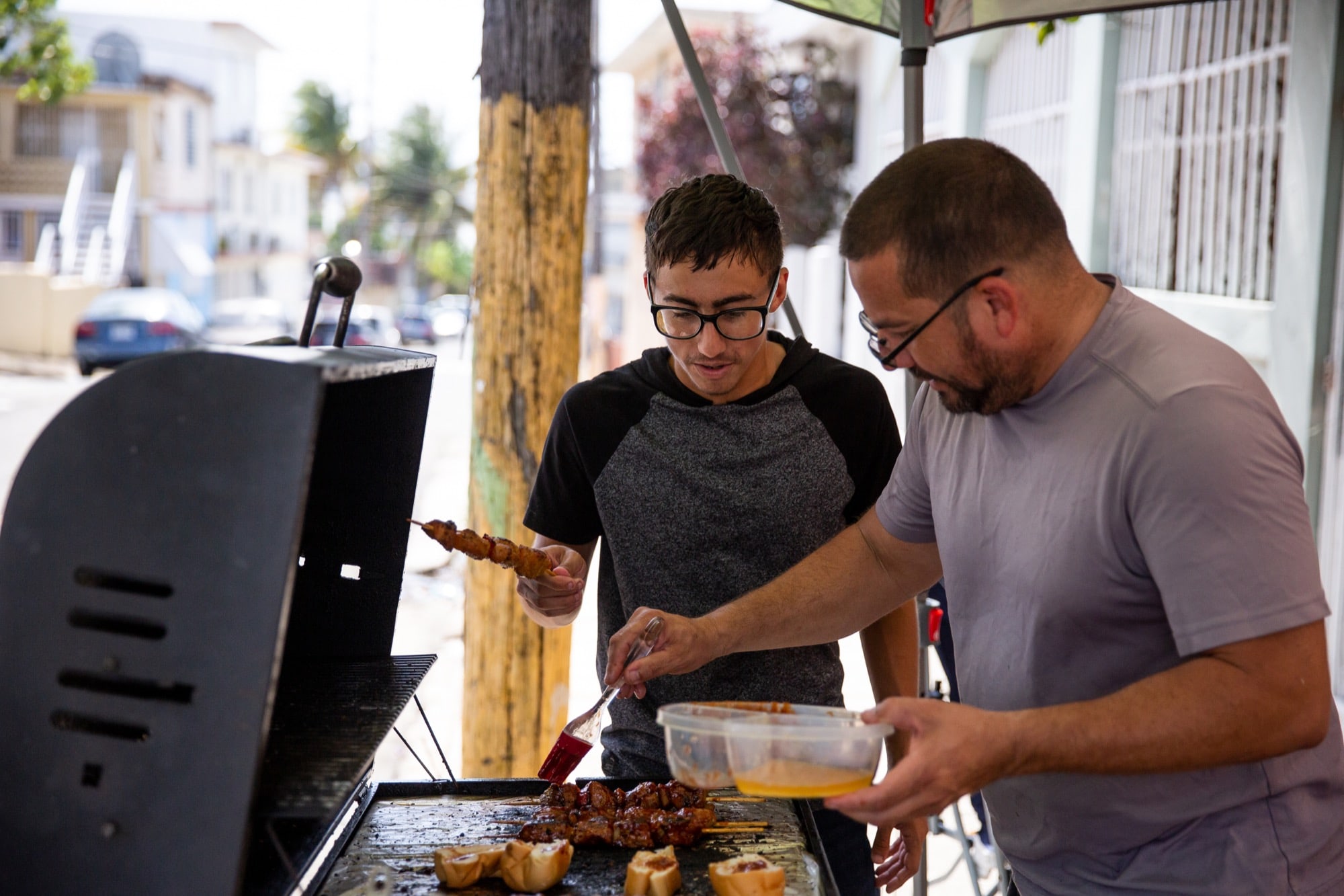 Ángel Morales Jr. (left) and his dad, Ángel Sr., make kebabs and hamburgers to sell in their neighborhood. The younger Morales said he tries not to think about the storm. (Ellen O'Brien/News21)